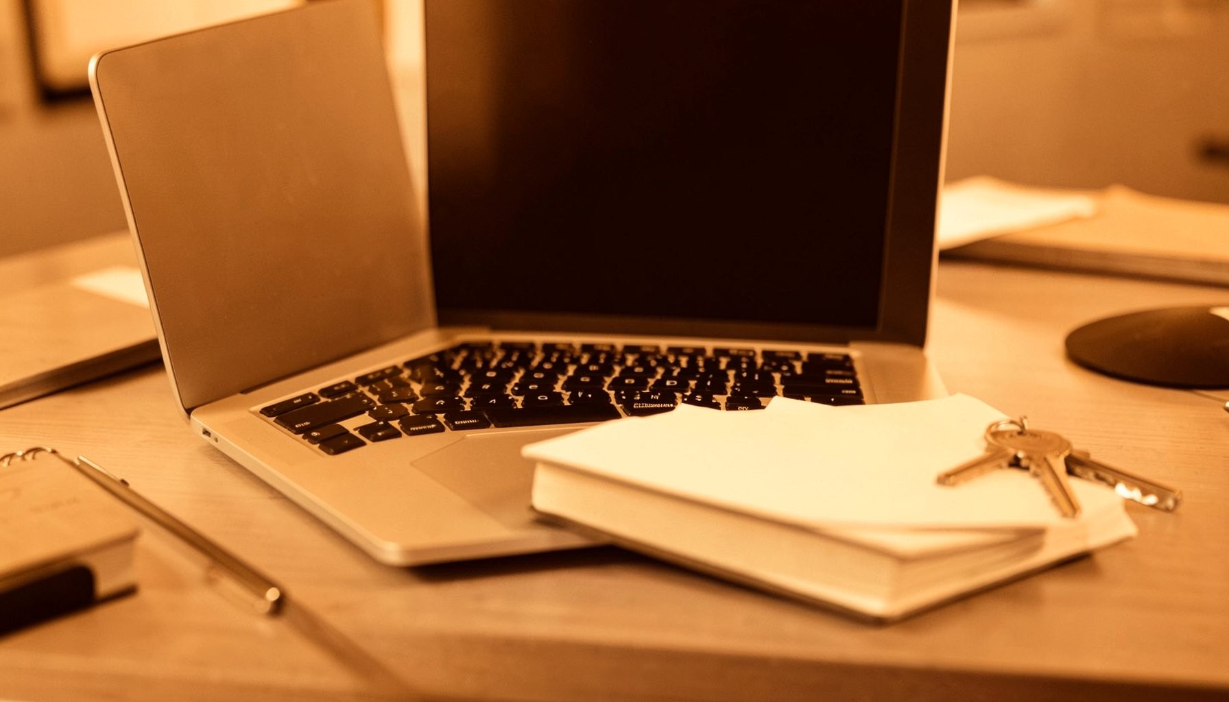 A duotone photograph of a neatly organized desk with a laptop, notepad, and keys, warm brown and cream tones, suggesting a professional real estate workspace.
