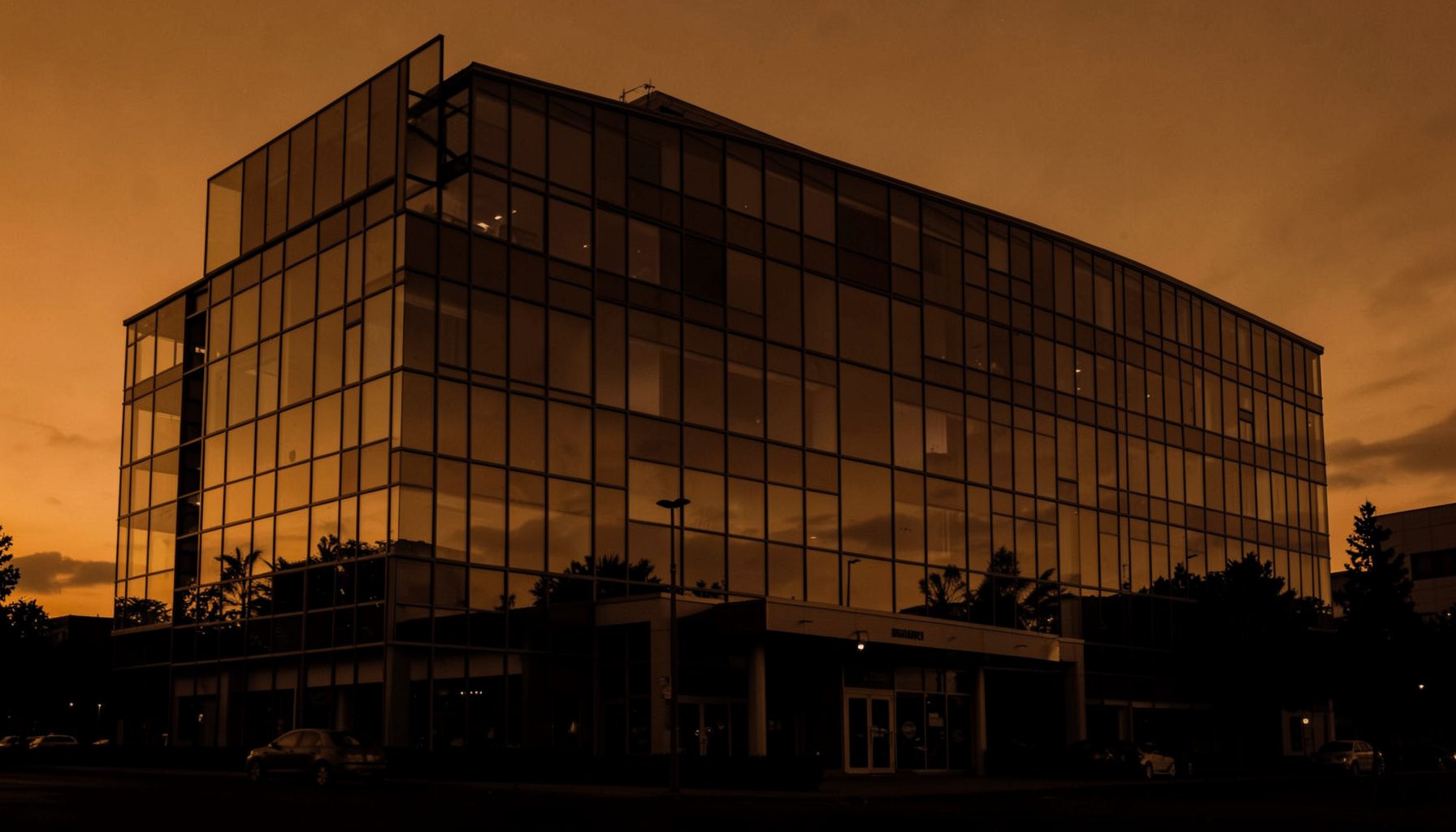 A warm duotone photograph of a modern glass office building facade at dusk, deep amber and charcoal tones, conveying professionalism and trust.