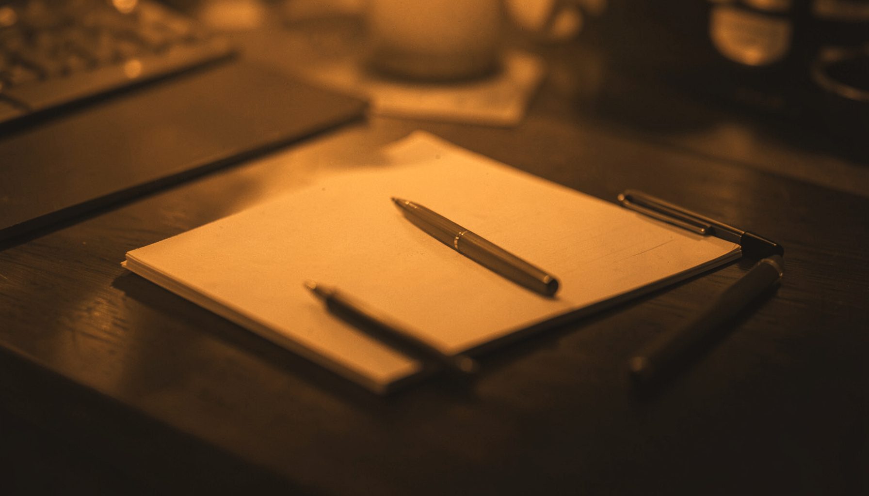 A warm duotone photograph of a modern desk with a notepad and pen, rendered in deep amber and charcoal tones, conveying a professional and approachable atmosphere.
