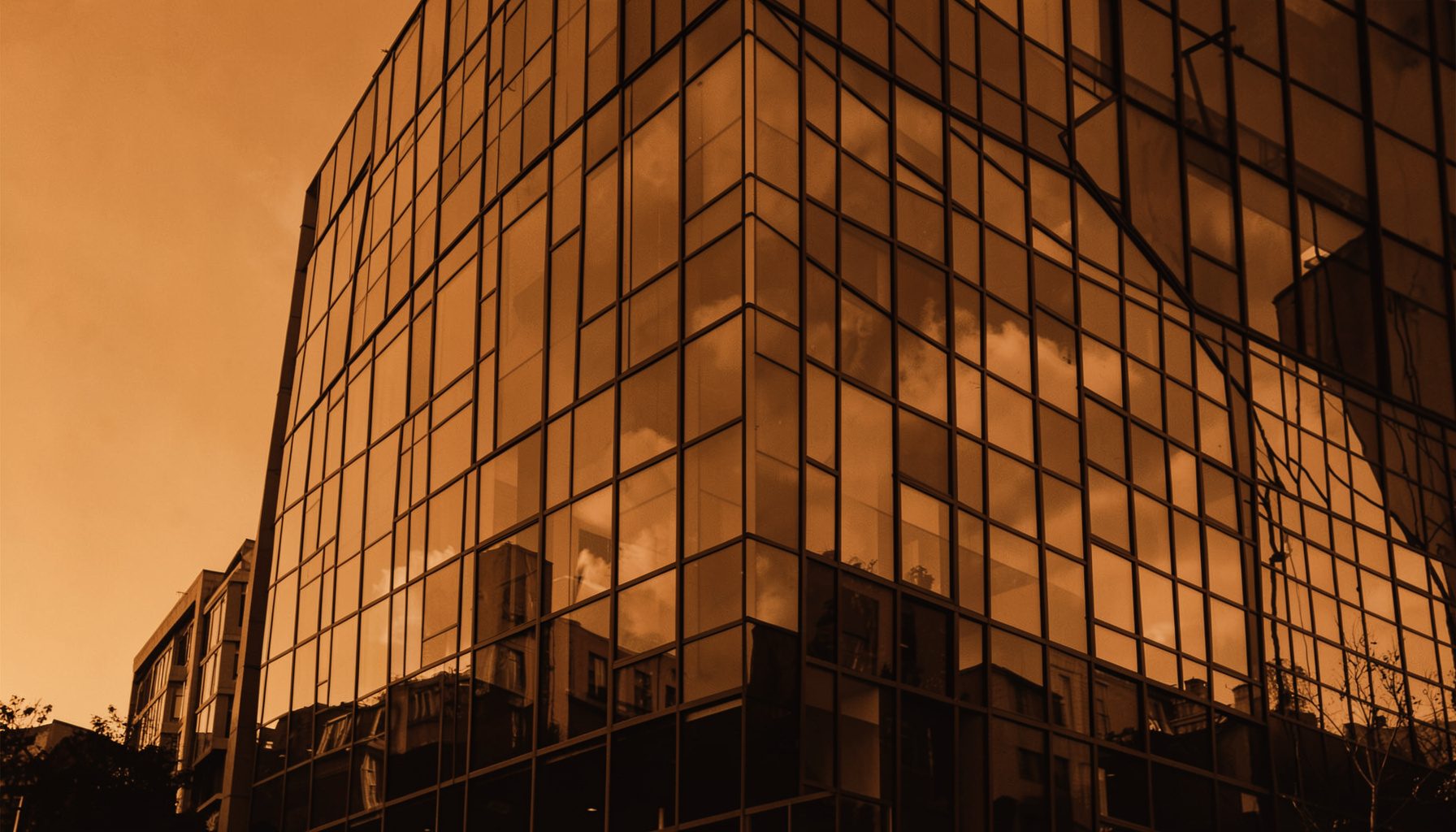 Warm duotone photograph of a modern glass office building facade reflecting soft amber and deep brown tones, conveying a professional and collaborative atmosphere.