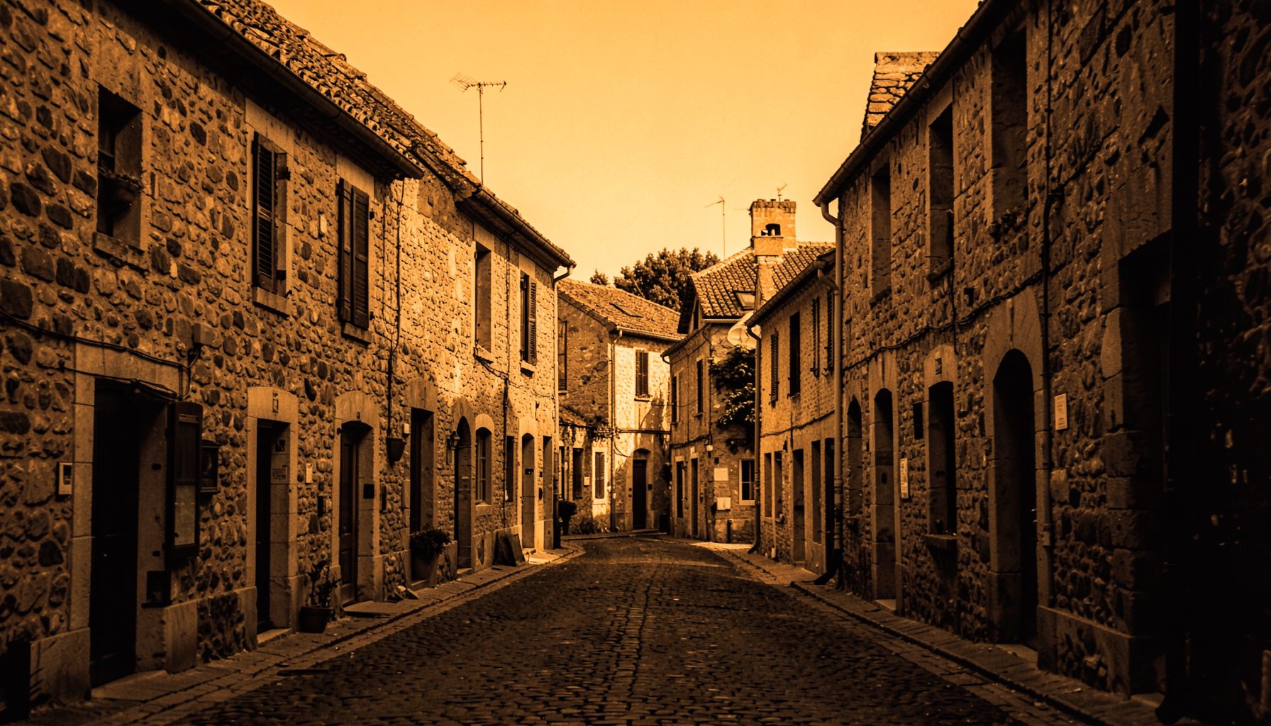 Warm duotone photograph of a sunlit French village street with stone facades and terracotta roof tiles, rendered in deep amber and charcoal tones